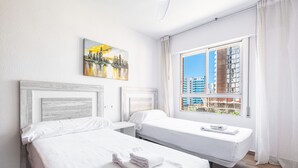 A hotel room with two beds, a large window with a city view, and a painting on the wall.