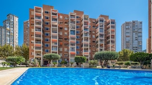 A swimming pool area with a view of multi-story residential buildings, surrounded by greenery and trees.