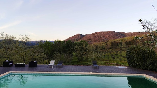 A pool area with lounge chairs and a view of a mountainous landscape.