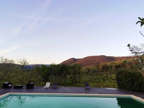Ett poolområde med solstolar och utsikt över ett bergigt landskap.