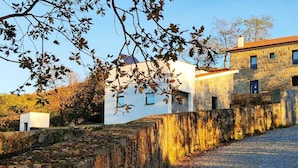 A stone wall with a cobblestone path leading to a white building with a red roof.