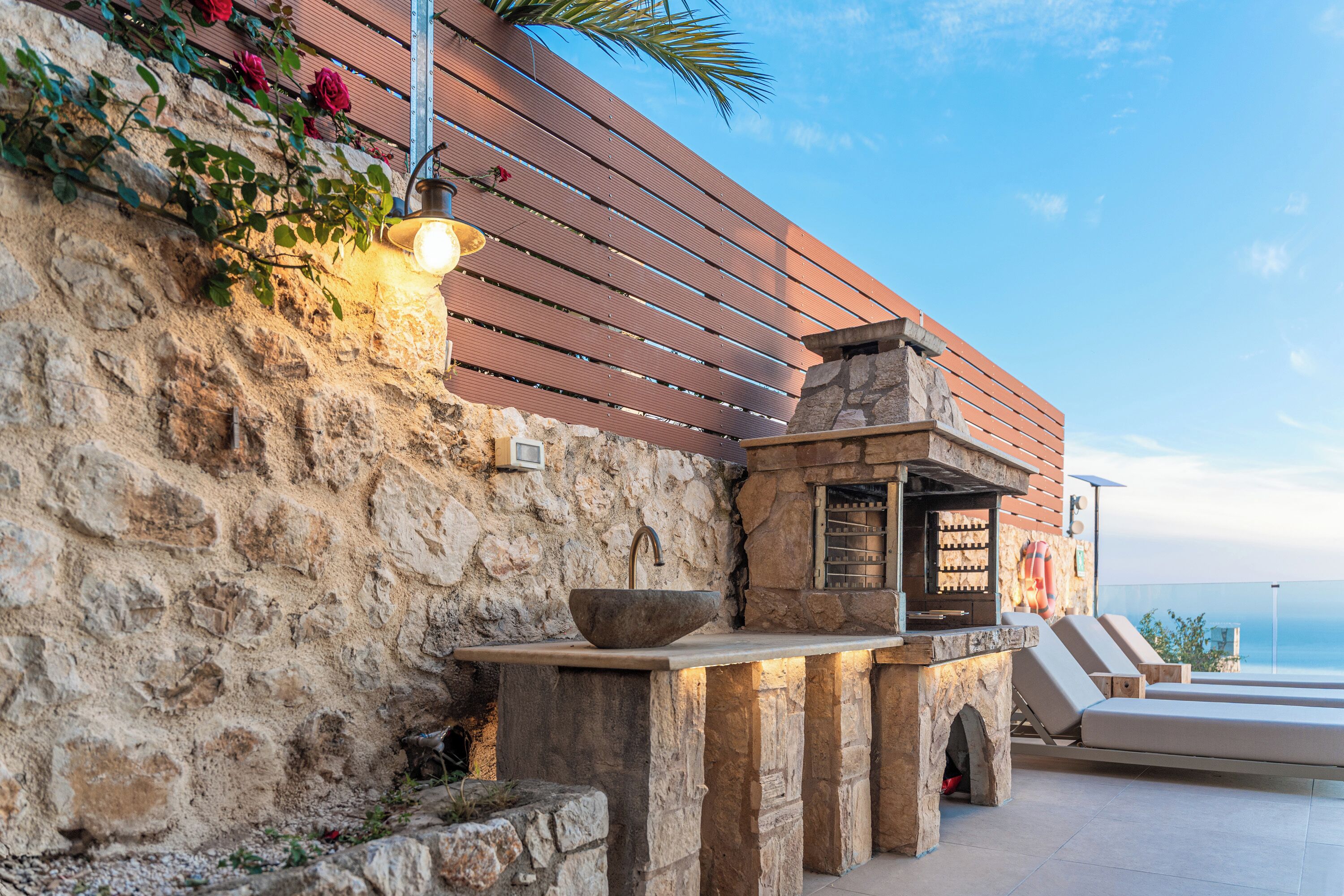 A stone wall with a wooden slat fence, a stone sink, and a bar area with a view of the ocean.