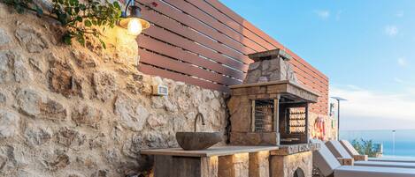 A stone wall with a wooden slat fence, a stone sink, and a bar area with a view of the ocean.