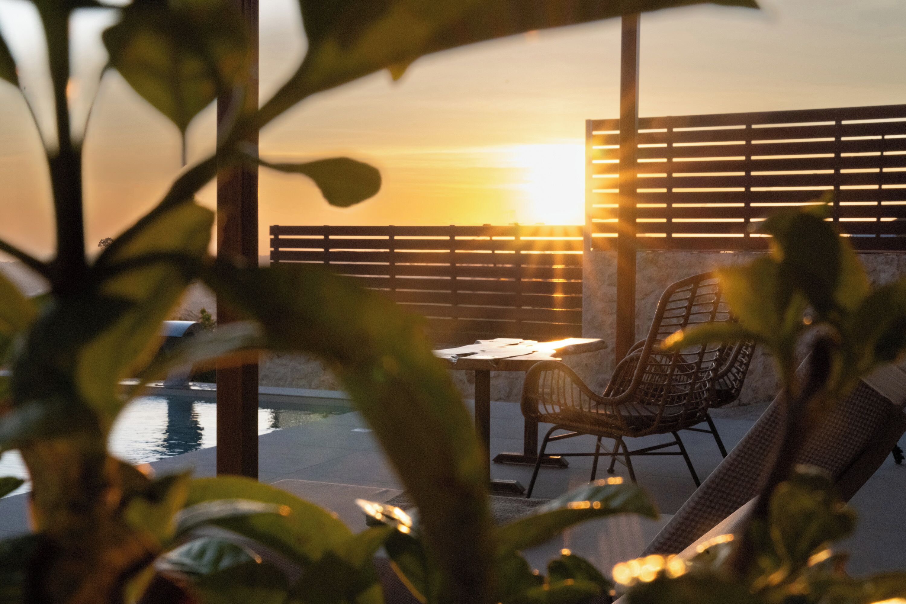 Una veranda con tavolo e sedie, vista su una distesa d'acqua, con un tramonto sullo sfondo.