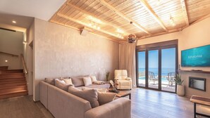 Een ruime woonkamer met een grote bank, een flatscreen-tv en uitzicht op zee door grote schuifdeuren.
