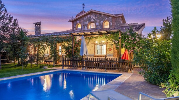 A poolside area with a stone building, a pergola, and a covered seating area.
