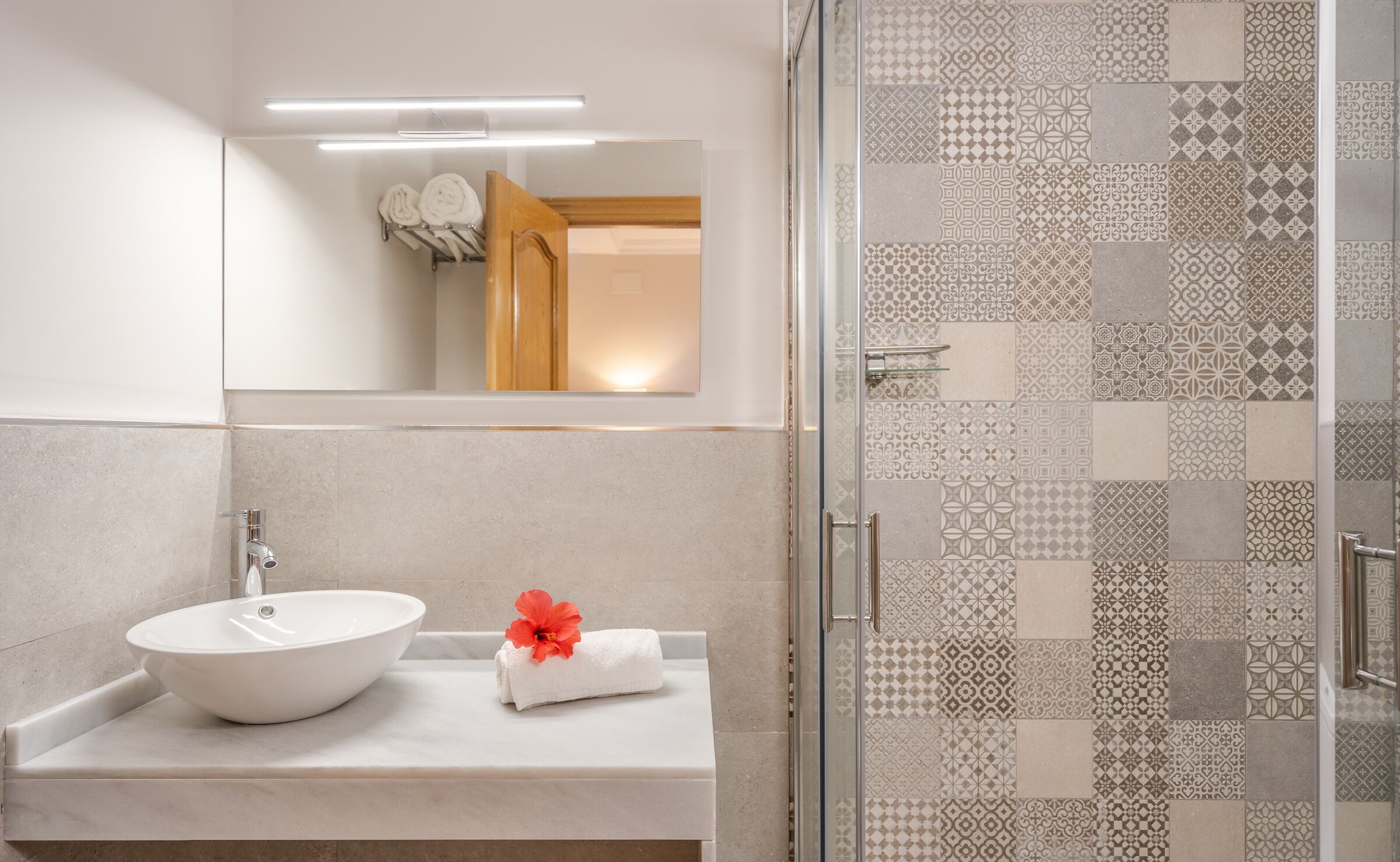 Un bagno moderno con un lavandino bianco, uno specchio e una doccia con piastrelle decorate.
