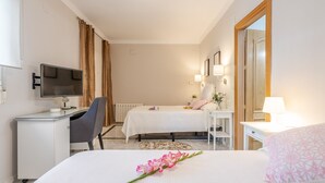 A hotel room with a bed, a desk, a chair, a TV, and a bedside table with a lamp.