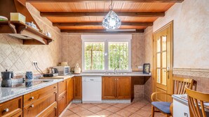 A kitchen with wooden cabinets, a white dishwasher, and a window with a view of greenery.