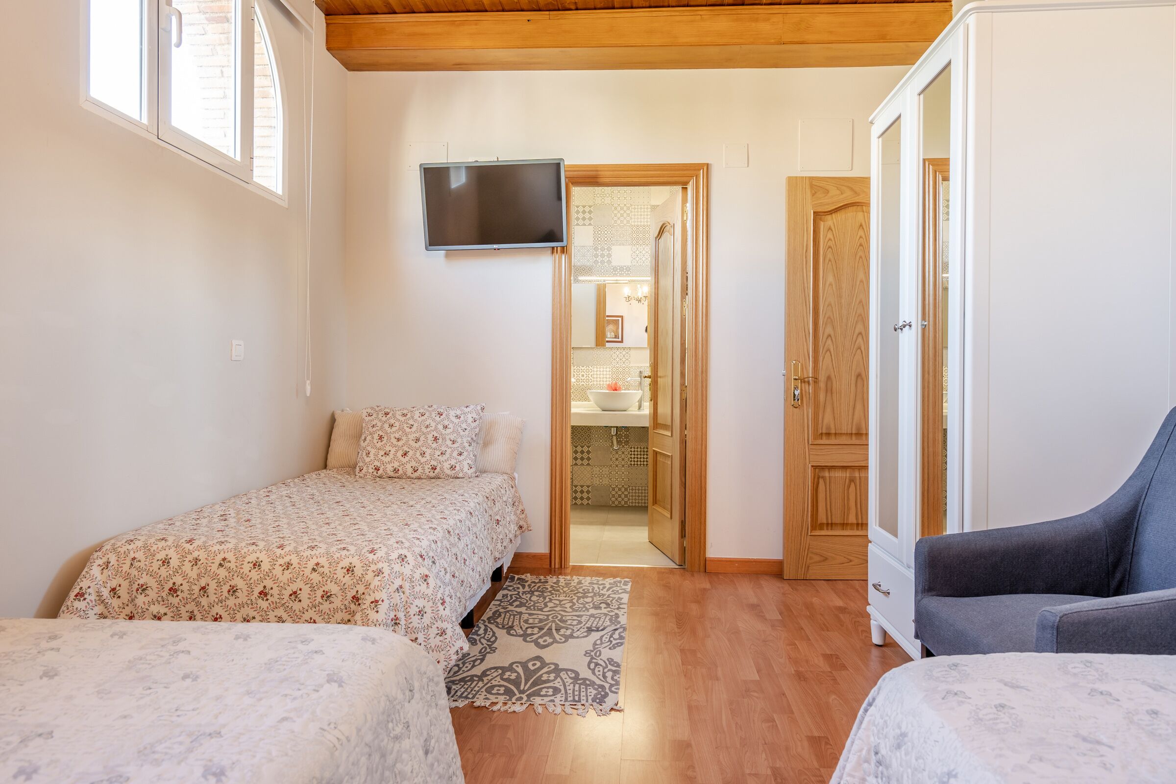 A bedroom with two beds, a TV, and a bathroom visible through an open door.