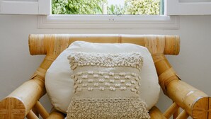 A room with a bamboo chair, a white cushion, and a view of palm trees through a window. - Farmhouse Finca Delicias La Canaria (Alcalá)