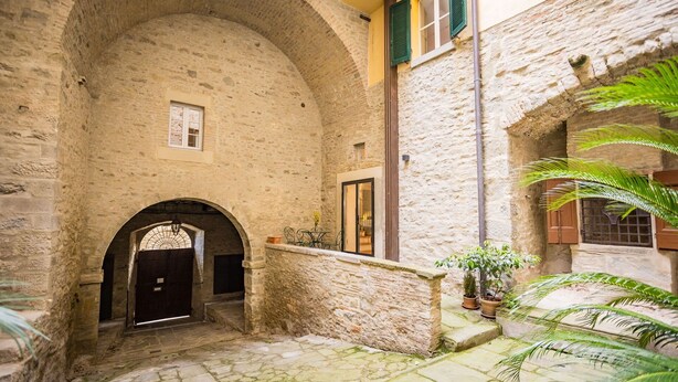 A stone courtyard with an arched entrance, potted plants, and a small table. - Appartamento La Corte (Cortona)
