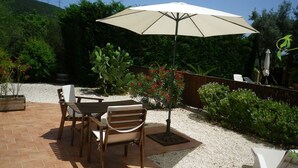 Eine Terrassengruppe im Freien mit Tisch und St ühlen, einem beige gefärbten Sonnenschirm und verschiedenen Pflanzen.