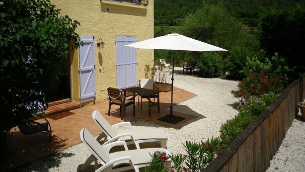 Eine Terrasse mit Tisch und Stühlen, einem weißen Sonnenschirm und Blick auf einen Hügel.
