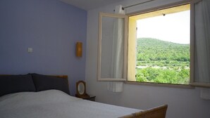 Ein Schlafzimmer mit einem Bett, einem Fenster mit Blick auf grüne Hügel und einer Wandleuchte.