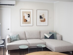 Een moderne woonkamer met een lichtgrijze modulaire bank, twee kleine ronde tafels en abstracte kunst aan de muur.