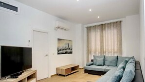 A modern living room with a flat-screen TV, a sofa, a coffee table, and a painting on the wall.