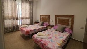 A hotel room with two beds, each with floral bedding and pillows, a wooden headboard, a nightstand, and a window with curtains.