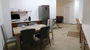 A compact kitchen with a dining table, chairs, a refrigerator, and a coffee maker.