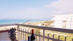 Une table avec une bouteille de vin, des verres et un panier de fruits, placée sur un balcon donnant sur une plage.