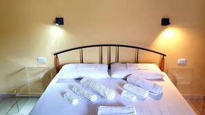 Un lit bien fait, avec des serviettes pliées en rouleaux, et une chaise en plastique transparente placée à côté.