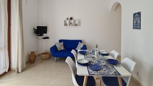 Un coin repas avec une table blanche dressée pour quatre personnes, un canapé bleu et un ventilateur de plafond.