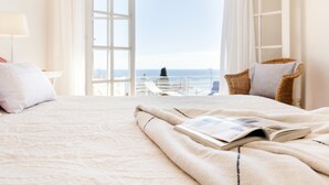 A bedroom with a large bed, a window with curtains, a wicker chair, and a view of the sea. - SAILOR HOUSE with SEA VIEWS (Tossa de Mar)