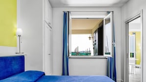Een slaapkamer met een bed, een raam met gordijnen, een lamp en uitzicht op het omliggende landschap.