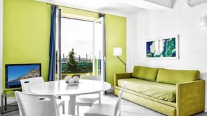 Een moderne woonkamer met een ronde witte tafel, witte stoelen, een groene bank en een groot raam met gordijnen.
