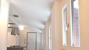 En smal gang med et tekøkken til venstre, en radiator til højre og en dør i enden.