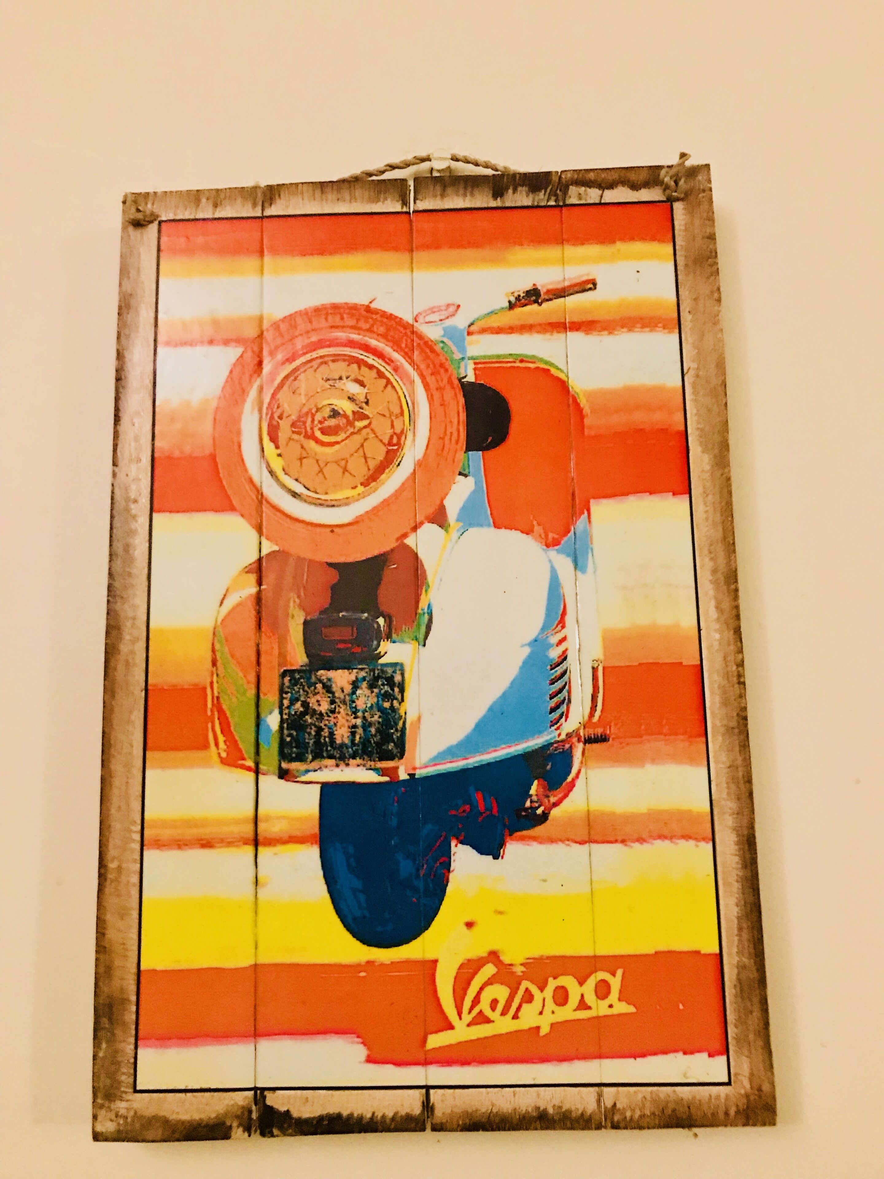 Uma pintura colorida de uma scooter com uma cesta e um capacete, emoldurada e pendurada na parede.