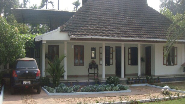 A two-story house with a tiled roof, a covered porch, and a garden with various plants and flowers. - Heritage Bungalow in Changanassery  (Changanassery)