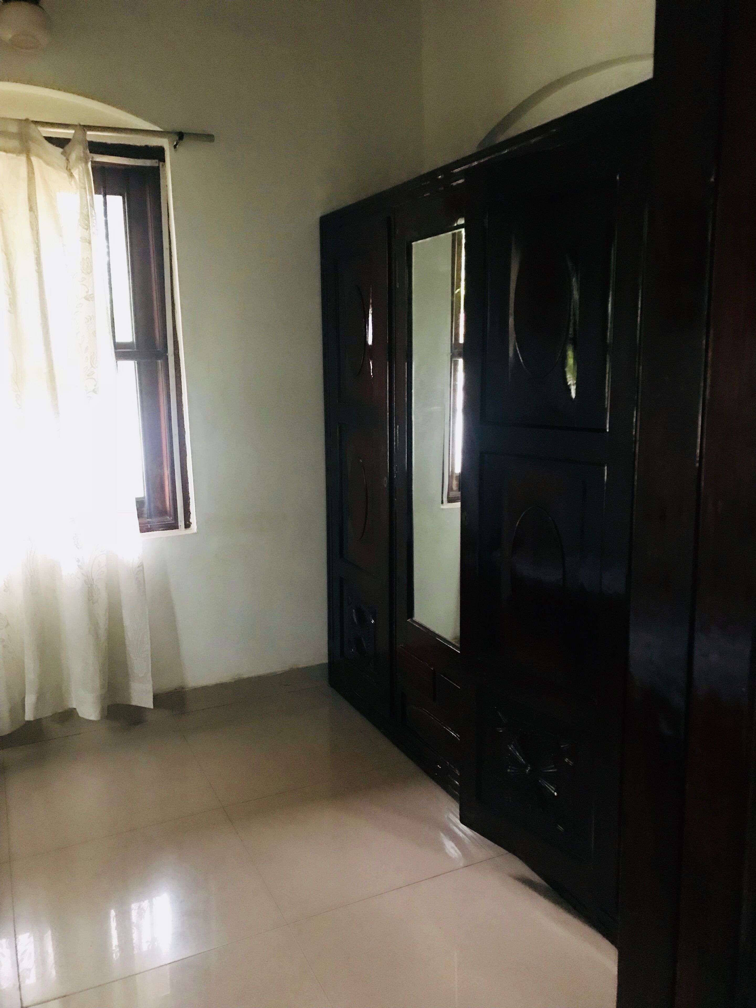 Quarto com guarda-roupa espaçoso, janela com cortinas e chão em azulejos.