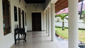 A covered corridor with white columns, a wooden bench, and a door at the end. - Heritage Bungalow in Changanassery  (Changanassery)