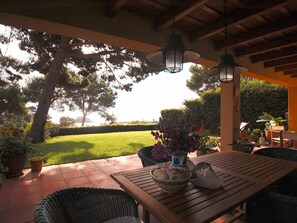 Un patio al aire libre con una mesa de madera, sillas de mimbre y faroles colgantes.
