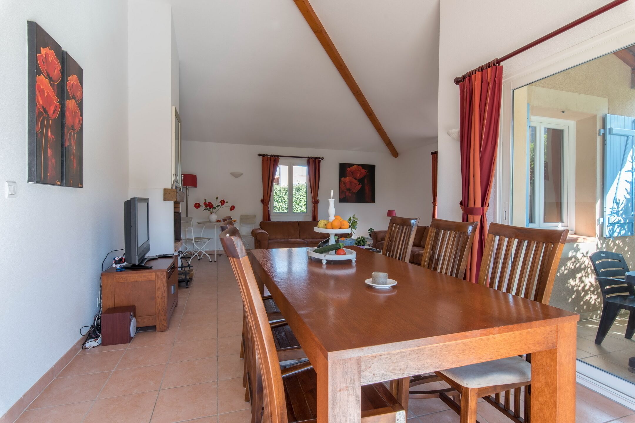 A dining area with a wooden table, chairs, a TV, and a fruit display.