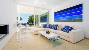 A modern living room with a white sofa, a glass coffee table, and a large abstract blue painting on the wall. - House with direct access to the sea, pool and wifi (Santanyí)