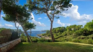 A coastal landscape with a stone wall, grassy area, and trees overlooking the sea. - House with direct access to the sea, pool and wifi (Santanyí)