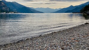 Un lac avec des montagnes en arrière-plan et une plage de galets au premier plan.