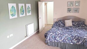 A bedroom with a bed, a radiator, and three leaf-patterned wall art pieces. - Garden flat, dog friendly, sleeps 3/4, enclosed garden, parking, level access (Tiverton)