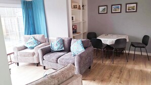 A living room with two sofas, a dining table with chairs, and a bookshelf. - Garden flat, dog friendly, sleeps 3/4, enclosed garden, parking, level access (Tiverton)