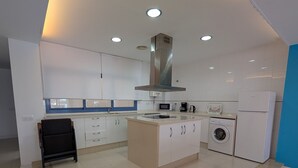 A modern kitchen with white cabinets, a central island, a stainless steel range hood, a microwave, a coffee maker, a washing machine, and a refrigerator. - 49 - Apartamento Sol Tarifa (Tarifa)