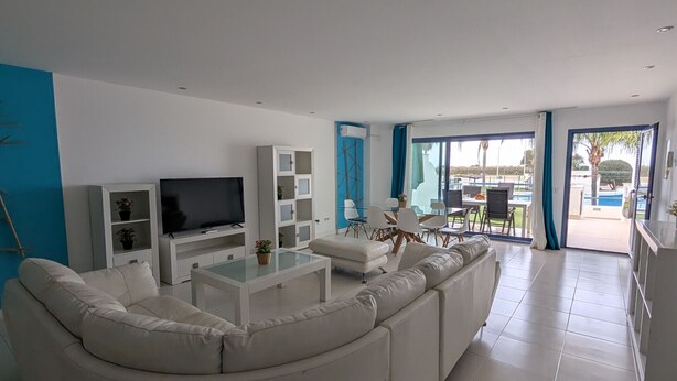 A modern living room with a white sectional sofa, a flat-screen TV, and a dining area with a table and chairs. - 49 - Apartamento Sol Tarifa (Tarifa)