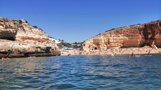 A coastal scene with rocky cliffs, a beach, and calm waters.