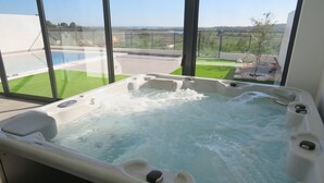 A hot tub with a view of a swimming pool and a green lawn.