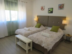 A bedroom with two beds, a bench, and a small table.
