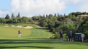 A golf course with a clear path, sand bunkers, and a clubhouse in the background.