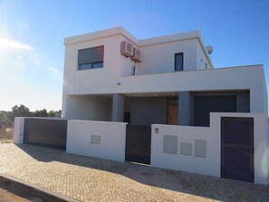 A modern two-story building with a flat roof, large windows, and a covered driveway.