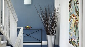 A hallway with a blue wall, a white railing, a black metal console table with decorative items, and a tall vase with branches. - Le Capannelle - Boheme by Feeling Italy (Massa Lubrense)
