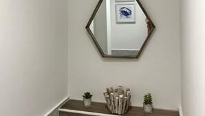 En hall med en sexkantig spegel som hänger på väggen, en liten växt och en dekorativ trädetalj på golvet.